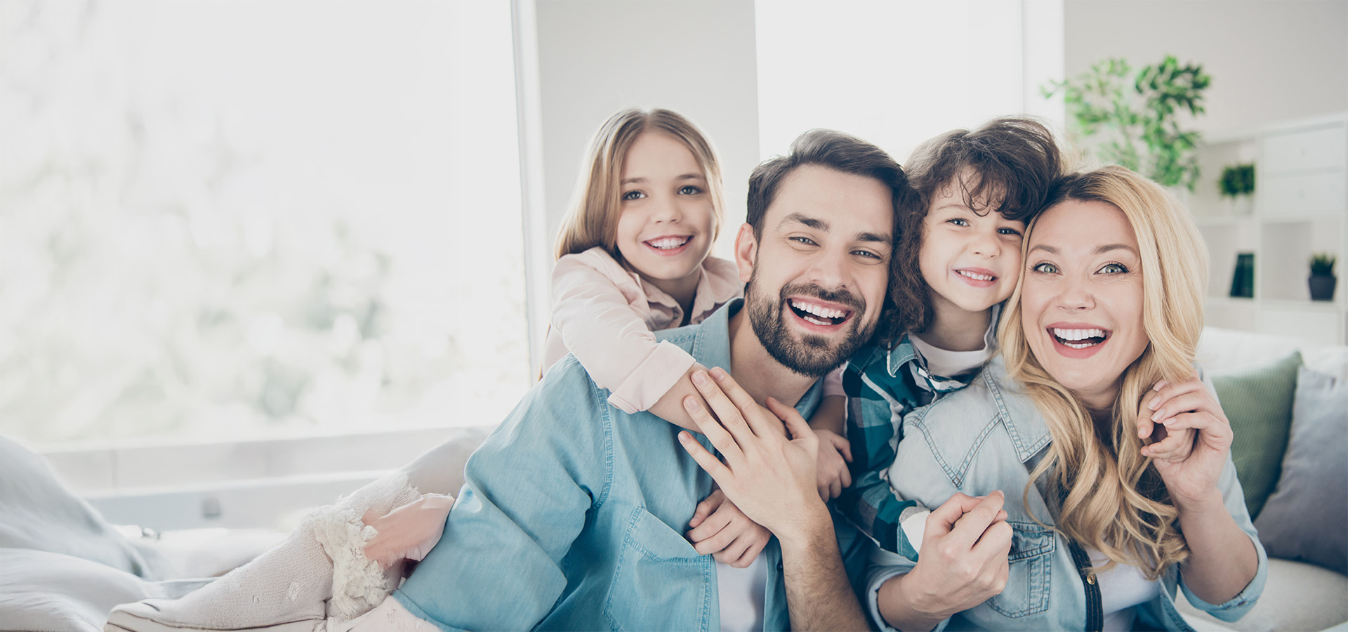 Eine vierköpfige Familie, bestehend aus Mutter, Vater, Tochter und Sohn, die gemeinsam in die Kamera lächeln,